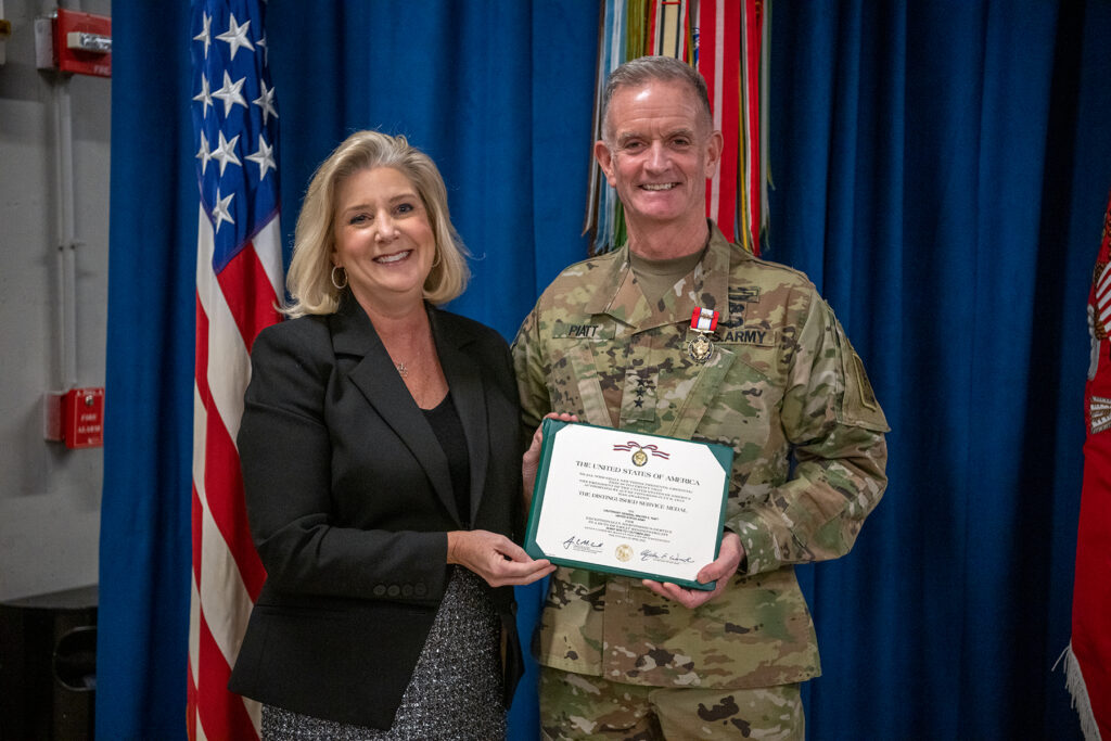 Walt Piatt and Christine Wormuth stand holding a framed Distinguished Service Medal certificate.